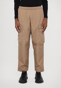 Beiga cargobyxor med elastisk midja, som har två sidfickor och ett strukturerat tyg. Bärs med svarta sneakers.