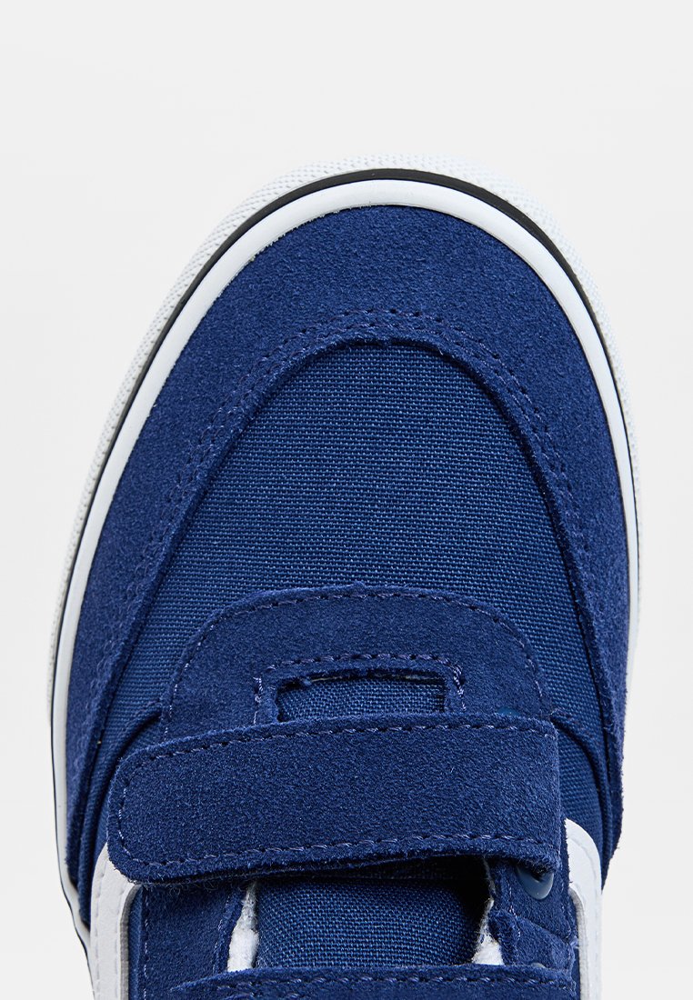 Blauwe sneaker van een combinatie van stof en suède. Voorzien van een klittenbandsluiting, ronde neus en een witte rubberen zool met zwarte accenten.