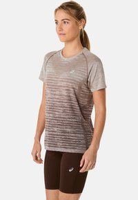 Koszulka sportowa w jasnobrązowym kolorze z gradientowym wzorem, z krótkimi rękawami i okrągłym dekoltem. Posiada siateczkowe akcenty oraz logo. W komplecie z ciemnobrązowymi szortami.