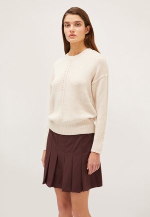 Lichtbeige gebreide trui met geribde onderrand en stiksels. Gecombineerd met een donkerbordeaux geplooide rok en lange mouwen.