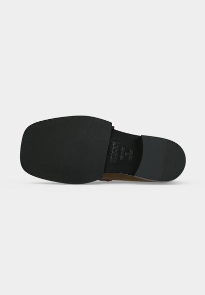 Σόλα από μαύρο παπούτσι τύπου slip-on με υφή για καλύτερο κράτημα και ανάγλυφο όνομα επωνυμίας, εμφανίζεται πάνω σε ουδέτερο ανοιχτό φόντο.