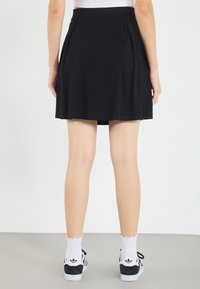 Zwarte geplooide rok met een aangesloten taille, gemaakt van zachte stof. Draagt witte sokken met een gekartelde rand en zwarte sneakers. Gladde textuur, tot aan de knieën.