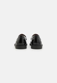 Scarpe in pelle verniciata nera con una superficie liscia, punta arrotondata e design minimalista; presentano un tacco basso e un dettaglio con cinturino alla caviglia.