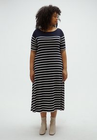 Tengerészkék és krémszínű csíkos pamut midi ruha rövid ujjakkal, kerek nyakkivágással és légies A-vonalú szabással, bézs bokacsizmával párosítva.