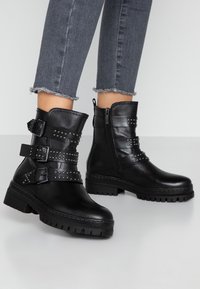 Zwarte enkelboots van leer, voorzien van meerdere gestikte banden en een zijrits, met een chunky zool en gestructureerde details.