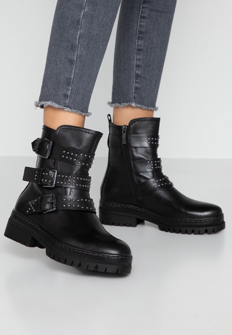 Zwarte enkelboots van leer, voorzien van meerdere gestikte banden en een zijrits, met een chunky zool en gestructureerde details.