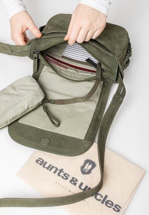 Sac bandoulière en daim vert avec fermeture éclair, intérieur rayé et poche intérieure zippée. Comprend une housse anti-poussière avec logo imprimé.