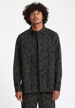 Camisa de botones verde oscuro con un patrón de murciélagos negros, hecha de una tela con textura suave, dos bolsillos en el pecho y un corte relajado.