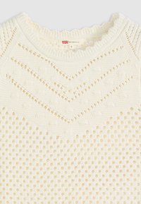 Maglione lavorato a maglia crema con un design a trama aperta e testurizzata, bordo a scallop sul collo e accenti a zigzag. Etichetta delle taglie visibile.