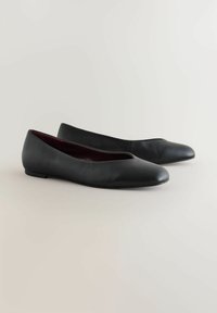 Musta nahkainen ballerinatyyppinen kengät, joissa on pyöristetty kärki, matala korko ja sileä pinta. Ominaisuuksiin kuuluu hienovarainen aukko-design lähellä etuosaa.