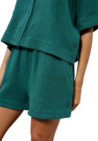Ensemble en mélange de coton bleu-vert comprenant une chemise à boutons ample et un short à taille élastique avec un tissu texturé et un logo brodé.