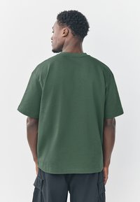 Grünes Baumwoll-T-Shirt mit lockerem Schnitt, kurzen Ärmeln und rundem Ausschnitt, mit glatter Textur und ohne sichtbare Logos oder Muster.