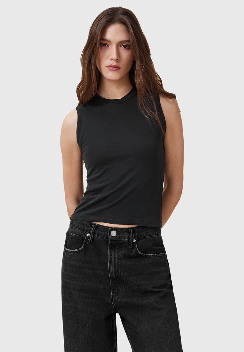 Sort ærmeløs top med høj halsudskæring, fremstillet af glat stof. Sammen med højtaljede sorte jeans med forlommer.