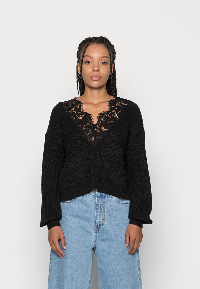 Sort strikket sweater med V-udskæring, der har en floral blondeindsats. Ærmerne er brede, og kanten er let cropped.