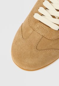 Baskets marron en daim avec dessus texturé, lacets crème et semelle en caoutchouc. Présentent des détails de couture et une conception à bout arrondi.