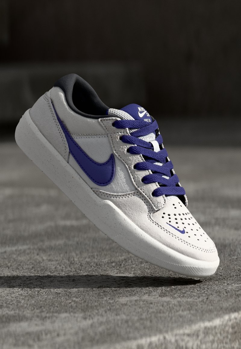 Nike tenisky s šedým koženým svrškem, fialovými akcenty, černým jazykem, perforovanou špicí a texturovanou bílou gumovou podrážkou.