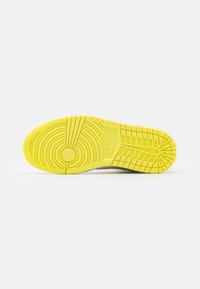 Yellow rubber sole of a Nike sneaker with circular and grid tread patterns, displayed flat against a white background.