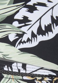 Čierny textil s tropickým vzorom listov v zelenej a bielej farbe. Textúrovaný povrch s sieťovými akcentmi na dolnom okraji.