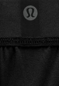 Melna sporta auduma tekstūra, ar savelkamu apakšējo malu un apļveida logo pelēkā krāsā.