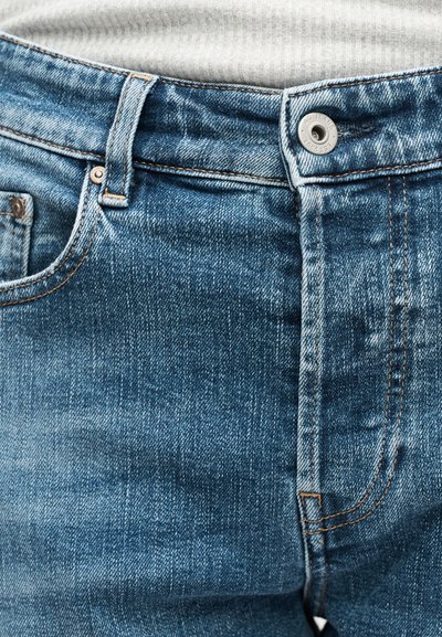 Κλείσιμο της μέσης μπλε τζιν με κουμπί στερεωμένο πάνω από μία λευκή υφασμάτινη ζώνη.