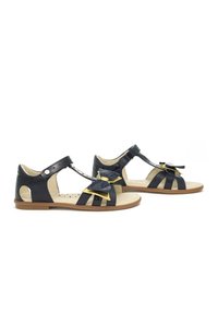 Sandali in vernice blu navy con lati aperti, caratterizzati da un grande fiocco e dettagli dorati, punta chiusa, cinturino alla caviglia regolabile e suola piatta.