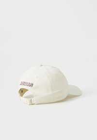 Hvit baseballcap med justerbar stropp, brodert "ADIDAS"-tekst i mørkerød på baksiden, vist fra venstre bakside.
