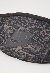 Schwarze Stoff-Hüfttasche mit einem strukturierten, dunkelgrauen Muster und einem auffälligen schwarzen Nike-Logo. Verfügt über einen schwarzen Reißverschluss.