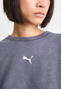 Sudadera gris hecha de una tela suave, con un escote redondo y un logo de Puma blanco en el pecho. Textura sutil con un aspecto usado.
