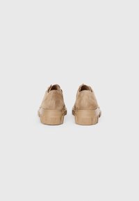 Sapatos de camurça castanho claro com uma sola de borracha espessa e texturada e bordas arredondadas, apresentando um design minimalista e sem hardware visível.