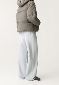 Šedá péřová bunda s kapucí, vybavená prošívanou texturou. Spojená s dlouhými světlými šedými džíny a černými teniskami pro volný styl.