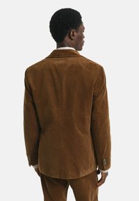 Blazer en velours côtelé marron avec revers standards, devant à deux boutons et coupe confortable. Présente une texture côtelée et un détail de dos ajusté.