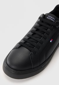 Czarne skórzane trampki z okrągłym noskiem, płaskimi sznurowadłami i gumową podeszwą. Posiadają małe logo oraz teksturowany wzór na podeszwie.