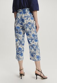 Cremfarbene, floral bedruckte Cropped-Hosen mit blauen botanischen Mustern, elastischem Bund und lockerem Schnitt, kombiniert mit schwarzen Riemchen-Absätzen.