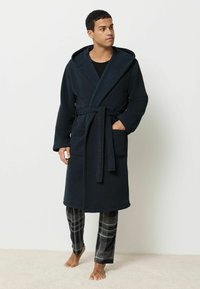 Námornícky modrý flísový župan s kapucňou, dvojitými vreckami a viazaným opaskom. Spárované s čiernymi a sivými károvanými pyžamovými nohavicami.