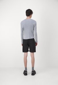 T-shirt gris à manches longues, ajustée et côtelée, avec un col rond, associée à un short cargo noir et des chaussures à plateforme noires, vue de dos.