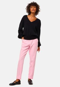 Pull-over noir en V, en matériau doux, coupe décontractée, associé à un pantalon tailleur rose clair, avec des jambes droites et des poches. Des chaussures noires complètent la tenue.