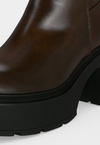 Gros plan d'une botte en cuir marron avec une semelle plateforme noire épaisse et un talon bloc solide.