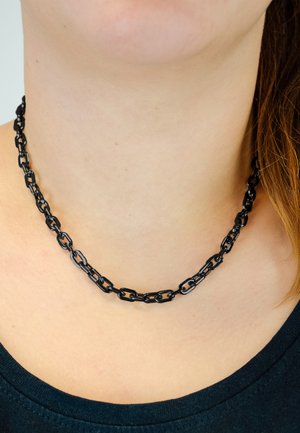 Zwarte ketting gemaakt van aaneengeschakelde metalen segmenten, met een gladde textuur en een uniform ontwerp, rustend op een blote nek.