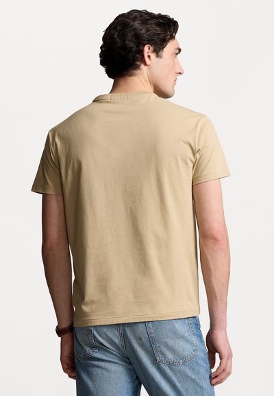 Tricou din bumbac bej cu mânecă scurtă și guler rotund, având o textură netedă și o croială lejeră, văzut din spate.