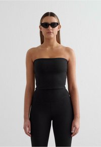Black strapless top made of soft fabric, paired with high-waisted black leggings. Model also wearing sleek black sunglasses.