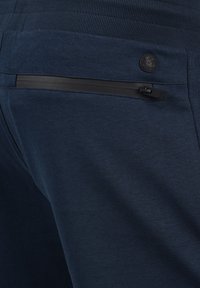 Navy blue jogger pants feature a textured fabric, elastic waistband, and a zippered pocket with a black zipper for secure storage.