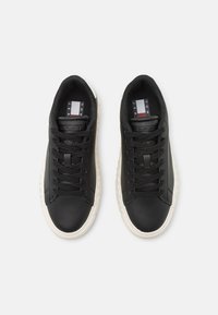 Zapatillas de cuero negro con una suela texturizada, cordones planos y una etiqueta de marca con franjas rojas, blancas y azules en la lengüeta.