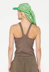 Top smanicato marrone con design a schiena scoperta, abbinato a pantaloni verde oliva. Indossa un cappello a motivi verdi e bianchi con dettaglio a sciarpa.