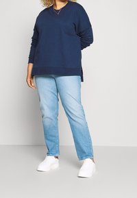 Felpa blu navy con maniche lunghe e scollo rotondo, abbinata a jeans a gamba dritta celesti e sneakers bianche.