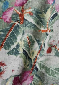 Blommig tyg med stora gröna blad och livliga rosa och röda blommor. Texturerad yta med en mjuk, vevrad utseende. Horisontella linjer är tydliga.