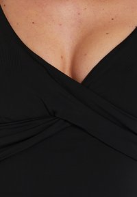 Top avvolgente nero realizzato in un tessuto testurizzato, con scollatura a V e dettagli arricciati sul seno, in una vista ravvicinata.