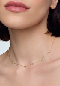 Złoty naszyjnik z łańcuszka z małymi, płaskimi okrągłymi i kulistymi akcentami, prezentowany na nagiej skórze, podkreślając jego delikatny design.