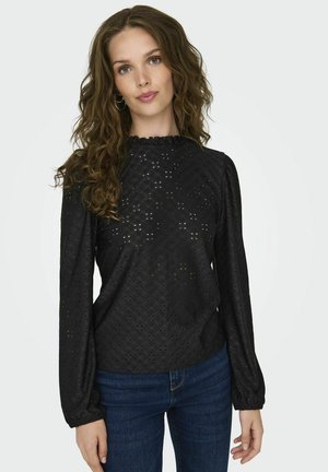 Black blouse featuring long puffed sleeves, ruffled neckline, and eyelet design, paired with blue denim jeans.
