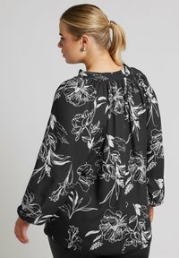 Blusa nera con motivo floreale bianco, vestibilità ampia, maniche lunghe, scollo arricciato e pantaloni plissettati sul retro, realizzata in tessuto leggero.
