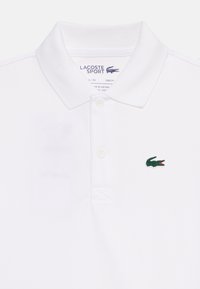 Λευκό αθλητικό πόλο Lacoste με δύο κουμπιά και μικρό πράσινο λογότυπο κροκόδειλου στο αριστερό στήθος.